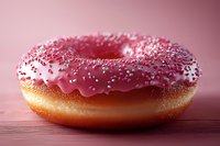 Fresh baked donut with pink strawberry glaze and white sprinkles on wooden surface against pink background, close up view for food photography.