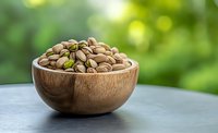 Fresh roasted pistachios in wooden bowl against blurred green natural background, selective focus on nuts creating appetizing healthy snack composition.