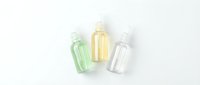 Three transparent plastic bottles with pump dispensers containing green, yellow and clear liquids isolated on white background for skincare and cosmetic design.