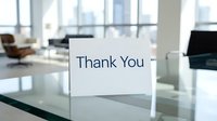 Thank you card standing on a glass desk in a modern office interior with city view, expressing gratitude in a professional setting.
