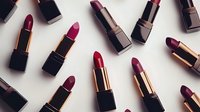 Luxury lipsticks in red and burgundy shades with metallic gold accents arranged on white background, flat lay composition for beauty and cosmetics marketing.
