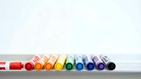 Colorful markers arranged in rainbow spectrum from red to black on white surface against light background for creative projects and artistic designs.