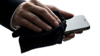 Young adult male with dark skin tone cleaning smartphone screen with microfiber cloth, isolated on white background for tech support and device care concepts.