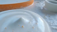 Fluffy white meringue peaks with orange zest scattered on white ceramic plate, close-up view showing soft texture and delicate swirls of whipped egg whites.