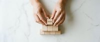 Female hands carefully placing wooden blocks to build tower structure on white marble surface representing business growth strategy and foundation building.