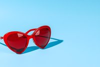 Red heart-shaped sunglasses casting shadow on bright blue background. Minimal summer fashion concept with copy space for seasonal accessories and style.