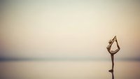 Woman practicing yoga pose on calm water surface during golden hour sunset creating peaceful meditation and wellness atmosphere.