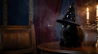 Black cat wearing witch hat sitting on wooden table in candlelit room with mystical atmosphere for Halloween decorations and spooky seasonal designs.