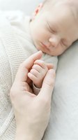 Peaceful newborn baby sleeping while parent gently holds tiny hand in tender moment of love and connection on soft knitted blanket.