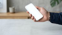 Man holding smartphone with blank white screen at wooden desk, displaying mobile device for app mockup and digital technology concepts.