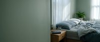 Cozy minimalist bedroom interior with unmade bed, soft natural lighting from windows, and green plant creating peaceful morning atmosphere for home decor.