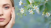 Young blonde woman touching face with white jasmine flowers for natural skincare and beauty wellness concept.
