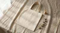 Natural cotton tote bag on linen fabric with eucalyptus branch and wooden spool in soft sunlight for eco-friendly shopping and sustainable lifestyle.
