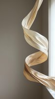 Elegant flowing silk ribbon in warm beige tones creating graceful spiral curves against soft neutral background for luxury fashion and textile design.