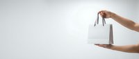 Female hands holding white paper shopping bag with handles against clean white background for retail and commercial design projects.