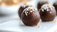 Dark chocolate truffles with coconut flakes and nuts on white surface, selective focus on foreground candy, macro food photography for confectionery marketing.