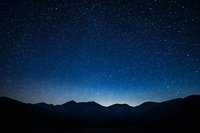 Majestic mountain silhouettes against deep blue night sky filled with countless stars, creating a serene cosmic landscape for astronomy enthusiasts.