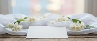 Blank white card mockup with jasmine flowers on white plates and soft bokeh background for wedding or event design.