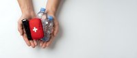 Male hands holding red first aid kit and water bottle on white background, representing emergency preparedness and healthcare support.