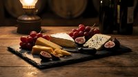 Assorted cheeses with red grapes and figs on slate board, wine bottles and lantern in background, gourmet food styling for entertaining and culinary content.