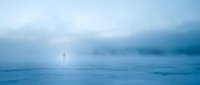 Young adult male figure standing alone in vast snowy landscape during blizzard conditions, surrounded by heavy fog and falling snow, conveying isolation and solitude in winter wilderness.