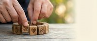 Wooden blocks with carved symbols being arranged by hands on rustic table surface with natural bokeh background for creative projects.