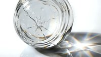 Cracked glass bowl with dramatic light reflections and prismatic effects on white surface creating abstract patterns and shadows.