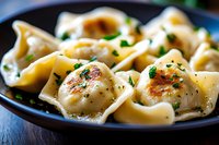 Pan-fried dumplings garnished with fresh herbs on dark plate, close up view showing texture and golden-brown sear marks, selective focus on steaming hot meal.
