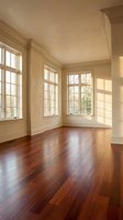 Empty room with hardwood floors and large windows creating warm natural light patterns on cream walls for interior design and real estate marketing.
