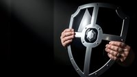 Businessman hands holding metallic security shield with lock symbol representing cybersecurity protection and data safety in corporate environment.