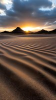 Dramatic sunset over desert mountains with rippled sand dunes in foreground, dark storm clouds and golden sunburst creating atmospheric desert landscape.