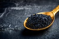 Black caviar on golden spoon against dark stone background, luxury gourmet food styling for restaurant menu and fine dining promotion.