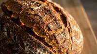 Freshly baked artisan sourdough bread loaf with golden crust and rustic scoring on wooden cutting board for bakery and homemade cooking concepts.