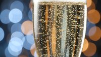 Champagne glass with golden bubbles against festive bokeh lights background for New Year celebration and holiday toasting moments.
