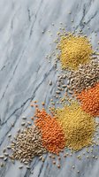 Assorted raw legumes and grains scattered on marble surface including lentils, millet, sunflower seeds creating colorful healthy food composition.