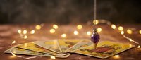 Mystical tarot cards spread on wooden table with crystal pendulum and warm bokeh lights creating atmospheric fortune telling scene for spiritual guidance.