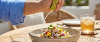 Young adult male hand squeezing fresh lime over colorful vegetable salad bowl at dining table, healthy eating and food preparation concept for nutrition and wellness content.