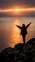 Woman with arms raised standing on rocky cliff overlooking ocean at sunset, silhouetted against golden sky with water reflection, expressing freedom and joy for lifestyle and wellness concepts.