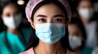 Asian female healthcare worker wearing protective surgical face mask and pink cap with blurred medical team in background. Focus on eyes expressing determination.