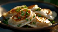 Pan-fried dumplings garnished with fresh chopped chives on dark ceramic plate, golden brown crispy bottom, soft steamed top, dramatic side lighting.