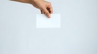 Hand holding blank white card or paper against neutral background for mockup and branding purposes.