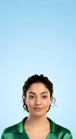 Young woman with dark curly hair and olive complexion wearing green shirt against light blue background for portrait and professional headshot use.