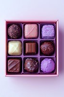 Luxury chocolate pralines and truffles in pink gift box. Assorted handmade bonbons with dark, milk, and white chocolate, decorated with purple glaze and sprinkles.