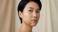 Asian woman with foundation makeup swatches on face showing different skin tones for cosmetic color matching and beauty product testing in natural light.