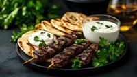 Grilled beef kebabs served with flatbread, yogurt sauce and fresh herbs on dark plate. Middle Eastern cuisine with traditional accompaniments and garnish.