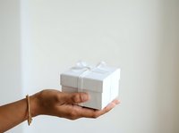 Cropped view of a person with medium skin tone holding a white gift box with ribbon bow, suitable for holiday, celebration, and retail marketing campaigns.