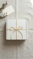 White gift box tied with gold ribbon on linen fabric, blank card and eucalyptus branch, flat lay for holiday or wedding styling.