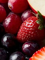 Fresh mixed berries macro shot showing juicy strawberries and dark purple grapes with water droplets in dramatic lighting, creating appetizing food composition.