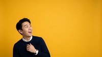 Young Asian male professional in dark sweater against bright yellow background, expressing excitement and enthusiasm with upward gaze, suitable for business and corporate marketing materials.