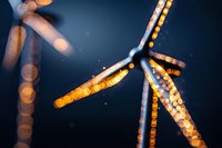 Wind turbine blades illuminated at night with golden bokeh lights creating dreamy atmospheric effect against dark blue sky. Modern sustainable energy concept.